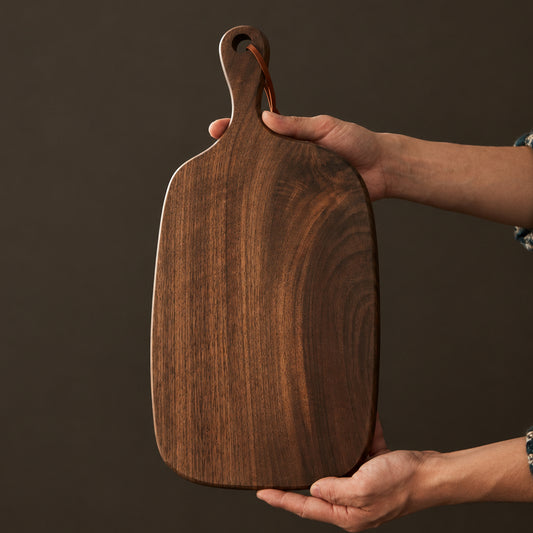 Wooden cutting board held by a hand with text on a brown background